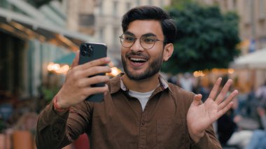 Mutlu, gülümseyen Hintli, etnik erkek, erkek, öğrenci, Z blogcu, modern cep telefonu kullanıyor. Gezici blog, cep telefonu, yurtdışındaki sosyal medyada el sallıyor.