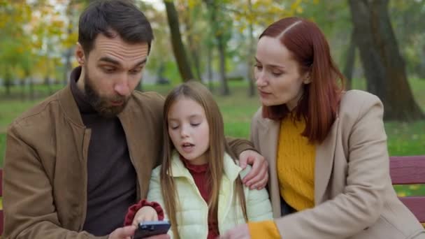 Kaukasiska Familjen Stadens Bänk Tillsammans Utomhus Höstpark Med Hjälp Mobiltelefon — Stockvideo