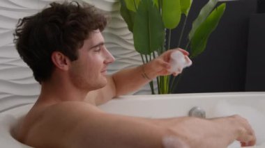 Kafkasyalı rahat bir adam evde banyo yapıyor sabah güzellik rutin hijyen prosedürü banyo köpüklü oyunda dinlenen erkek köpük üflüyor sıcak suyun tadını çıkarıyor hafta sonu küvette sıcacık suyun tadını çıkarıyor