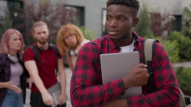 学生の多種多様なクラスメイトは アフリカ系アメリカ人の孤独な男の学生の下に親指を示す差別的なアフリカの大学で恥ずかしがり屋で恥ずかしがり屋を嘲笑する 問題を研究する男の教育 — ストック動画