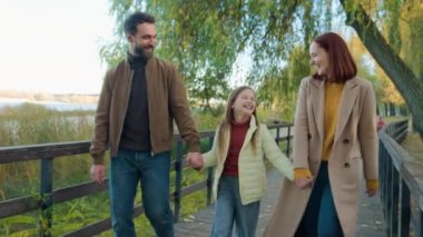 Beyaz mutlu aile tatili doğada, gülerek gülerek şehrin sonbahar parkında. Dost canlısı kız evlat çocuk. Anne babasıyla el ele yürüyecek.