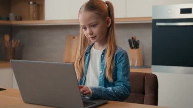 Küçük beyaz liseli kız bebek okul kızı. Ev mutfağında dizüstü bilgisayarı kullanan kız öğrenci. Web sitesi çocukları ve modern teknoloji nesli.