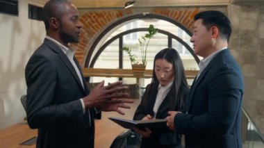 Afrikalı Amerikalı iş adamı Koreli Asyalı erkek meslektaşlarıyla konuşuyor. İki erkek çok ırklı iş adamları takım çalışması Japon kadın iş kadını sekreteri belgelere bakıyor.