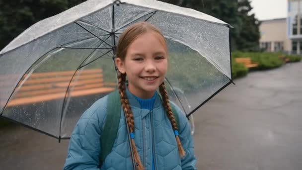 红头发的小女孩站在透明的伞下微笑着转过雨城公园外散步走着童年时代的天气新鲜的空气消遣大自然秋天的女儿女孩回到了学校 — 图库视频影像