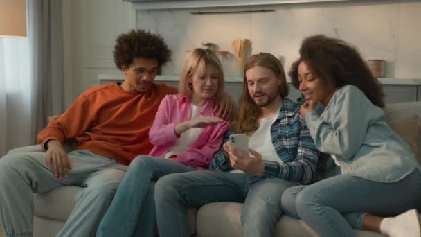 多种族的朋友多种族的人在一起用手机应用社交媒体指指指点点会笑的男人白人朋友非洲裔美国女孩坐在家里的沙发上 — 图库视频影像