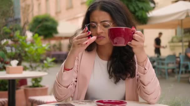 不快乐的年轻印度裔女孩喝咖啡时 会感到恼怒 因为她们在城外的街道咖啡店外使用了消极的信息通知手机 超负荷工作问题在线小工具错误问题 — 图库视频影像