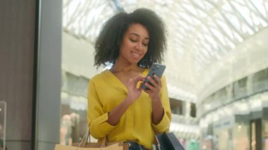 Cep telefonlu alışveriş merkezine gülümseyen mutlu Afro-Amerikalı kadın paketçi kızla mesajlaşıyor. Mesajlaşma, sevinç alıcısı Kara Cuma internetteki etnik sohbet.