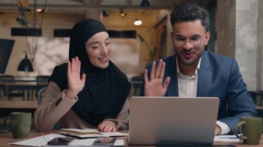 Arap Müslüman iş kadını Hintli işadamı iki iş ortağı tesettürlü kadın mutlu adam videosu konuşuyor bilgisayardan bilgisayara el sallayarak ofis içi iletişim toplantısını selamlıyorlar.