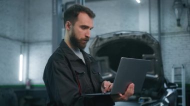 Profesyonel tamirci, üniformalı erkek, endüstriyel, makine mühendisi. Dizüstü bilgisayarı kullanarak otomobil kontrolü otomobil sistem mühendisliği araba bakımı hizmeti veriyor.