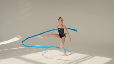 Beyaz stüdyo dans spor jimnastik okulunda jimnastik kurdelesiyle dönen sanatçı küçük kız, beyaz çocuk, kız öğrenci, balerin, kadın jimnastikçi, koreografi.