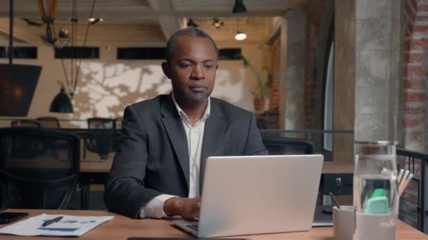 非洲裔美国中年企业家打字笔记本电脑族裔笑容满面的生意人办公室商人与Pc在线工作的男人在桌子边微笑着在镜头前健康地工作 — 图库视频影像