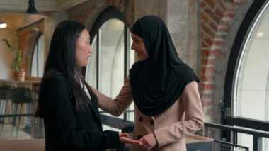 İki iş kadını kadın çok ırklı iş kadını Asyalı Koreli Çinli Çinli işçi dostça konuşuyor ofis arkadaşları arasında tesettürlü Arap Müslüman kadınla gülüyorlar.