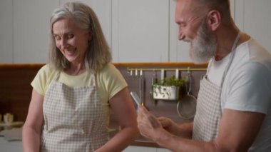 Kafkasyalı evli yaşlı çift mutlu aile olgun emekli kadın adam mutfakta birlikte kahvaltı hazırlıyor gülümseyen koca cep telefonu tutuyor fotoğraf karısına yemek bloğu yaptırıyor.