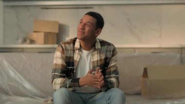 Neşeli etnik Afrikalı Amerikalı erkek kiracı kanepeye oturup gülümsüyor mutlu erkek ev sahibi yeni bir eve taşınmanın keyfini çıkarıyor daire kiralama, ev yenileme ve emlak kredisi alıyor.