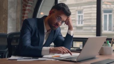 Arap Hindistanlı yorgun, üzgün iş adamı çalışanı. Masaüstü bilgisayarında sıkılmış, tembel, endişeli, iş adamı, iş adamı tükenmiş. Birlikte çalıştığı kafede sıkıcı, çalışan bir dizüstü bilgisayar yazıyor.