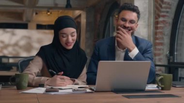 İki iş arkadaşı Arap Müslüman iş arkadaşları tesettürlü İslamcı kadın mutlu gülümseyen iş kadını iş kadını görüntülü görüşme görüntülü konferans sohbet laptopu ofiste