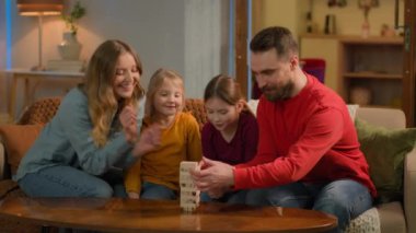 Mutlu bir aile, beyaz bir ebeveyn, anne ve baba çocuklarla oynuyor, tahta bloklar inşa ediyorlar, küçük anaokulu çocukları, kız kardeşler, kız kardeşler, evde oyun oynuyorlar, ilkokul eğitimi alıyorlar, çocukluk çağını öğreniyorlar.