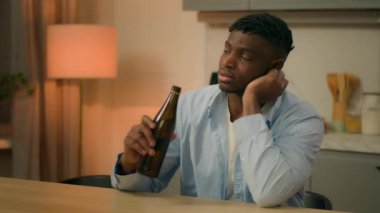 Sad upset African American man alone thinking at table in kitchen night drunk male addicted guy alcohol addiction drinking beer at home evening trouble pensive health problem alcoholism bankruptcy