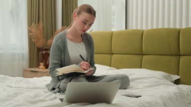 Caucasian student girl home education e-learning teenager female freelancer business woman at bedroom on bed writing notes study learning watching webinar class lesson online laptop write test prepare