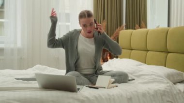 Angry stressed woman businesswoman multitasking girl female working online studying at home bedroom bed with laptop computer papers notebook talking mobile phone call argue freelance business problem