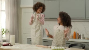 African American ethnic family mother woman mom babysitter with child kid daughter little girl chef having fun joy at home kitchen dancing together dance moving to music funny fooling cooking baking