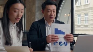 Business video call in office two partners Asian coworkers colleagues talking conference statistic diagram growth Korean Japanese woman girl female businesswoman with Chinese male guy man businessman
