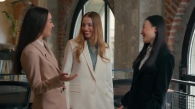 Three diverse business women friendly smiling laughing happy girls multiracial female multiethnic businesswomen Asian Korean Caucasian colleagues co-workers in office ladies together talking informal