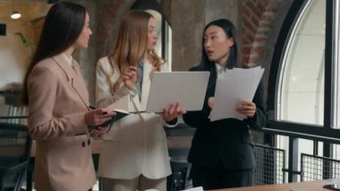 Group corporate brainstorm business women three multiracial multiethnic females diversity businesswomen Asian Caucasian girls in office documents laptop discuss talking planning sales online teamwork