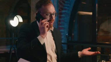 Dissatisfied confused puzzled businessman Caucasian office business man guy male work at dark night evening overtime talking mobile phone call smartphone discuss problem overworked CEO talk telephone