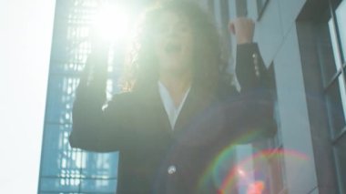 Happy winner excited Caucasian business girl joyful student woman businesswoman female in sunbeams outdoors winning success win achieve yes gesture celebrate achievement shout scream in city sun light