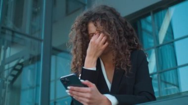 Tired Caucasian business woman girl businesswoman exhausted unwell ill girl hold smartphone looking at mobile phone screen feel pain rubbing dry eyes eyestrain headache blurry vision outdoors in city