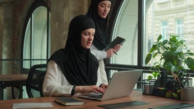 Başörtülü Müslüman bir kadın üzgün bir çalışan, dizüstü bilgisayarda çalışan Arap lider danışman eğitmen stajyer konuşma hatası sorununu iş projesiyle ilgili iki müslüman kadın işkadını iş kadınına öğretmeye geliyor.