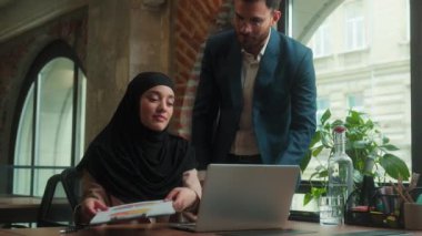 Müslüman İslami kadın tesettüre girmiş iş kadını dizüstü bilgisayarında çalışıyor Arap erkek işadamı iş adamı kontrol belgesi hata hata patron memnun değil ofis çalışanlarını üzüyor