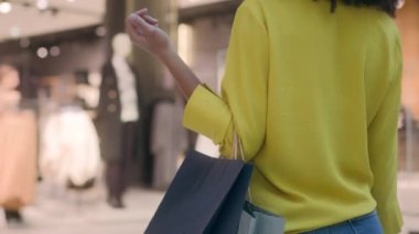 Arkaya bakan kadın elinde kağıt torbalarla alışveriş merkezine gidiyor. Alışverişe özgü moda bir siyah cuma kazağı alıyor. Yeni elbise mağazası indirimi yapıyor.