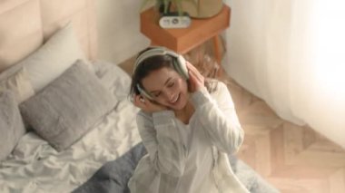 Yatakta dans eden enerjik bir kadın cep telefonu akıllı telefon ev kulaklıkları müzik teknolojisi aktif kız hafta sonu eğlence şarkıları söyleyen pozitif kiracı.