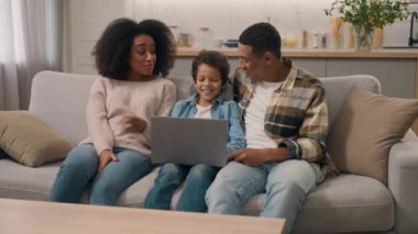 Modern laptop kullanan mutlu bir Afro-Amerikan ailesi. Anne, kadın, baba, baba, erkek, çocuk, çocuk, oğul çevrimiçi eğitim, not defteri, ev ödevleri, ev ödevler.