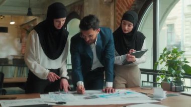 Arap erkek Müslüman kadınlar tesettüre girmiş iş arkadaşları mimar mühendis tasarımcı bina planı çiziyor kağıdın üzerine bina planı taslağı çiziyor ofiste tasarım mimarisini tartışıyorlar