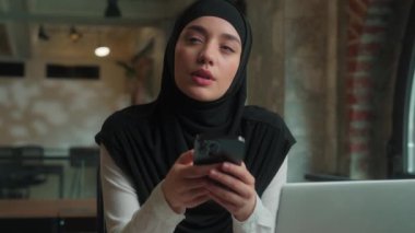 Düşünceli İslami Müslüman kız Arap iş kadını, tesettürlü kadın işkadını ofis çalışanı. Hayal kurmayı düşün. Cep telefonu yazma fikri, akıllı telefon.
