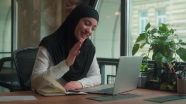 Arap müslüman iş kadını tesettürde mutlu gülümseyen iş kadını iş kadını kız öğrenci online sohbet videosu laptop konferansı selamlama selamlama merhaba yazışma notları ofis kafede