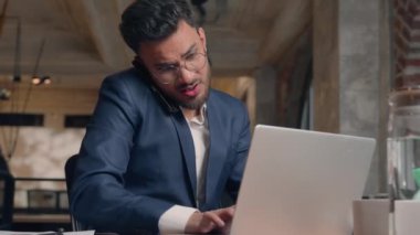 Stresli çoklu görev sahibi işadamı Hintli Arap erkek işadamı işveren müdürü danışmanı cep telefonuyla konuşuyor bilgisayarla ilgili belgeler yazıyor iş adamı sorunu fazla mesai