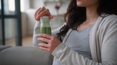 Sağlıklı, mutlu, hamile bir kadın. Kanepede hamile, yeşil organik meyve suyu içiyor. Mineral vitamin dengesi.