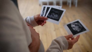Tanımlanamayan bir çift, ultrasonda hamilelik testi fotoğrafı seyrediyor. Evde USD fotoğrafları var. Evde kimliği belirsiz erkek, hamile, kız, erkek, anne, baba, bebek bekliyor.