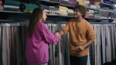 Çok ırklı mutlu beyaz kadın müşteri Arap Hintli erkek moda tasarımcısı konuşuyor kumaş mağazasında el sıkışıyor ortaklık anlaşması imzalıyor erkek tokalaşması tekstil atölyesinde