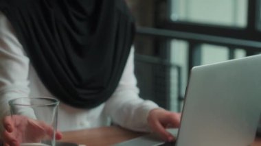 İslami kadın tesettürlü Müslüman iş kadını ofis masasında dizüstü bilgisayarda çalışan Arap iş kadını kadın yönetici bir bardak su içen susuz içki içen mutlu bir gülümseme