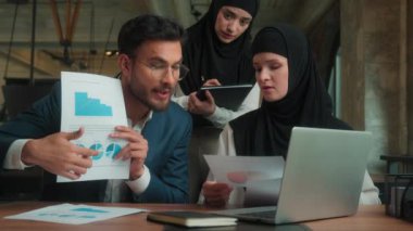 Arap Hindistanlı işadamı öfkeli bir konuşma videosu sunumundan memnun değil. Laptop konferansı sunumunda tesettürde çalışan Müslüman kadınlarla çalışan grafiker adam görülüyor.