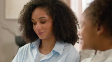 Afro-Amerikan mutlu kadın küçük kız aile psikologu gülümseyen etnik ev öğretmeniyle konuşuyor sohbet ediyorlar anne kız kardeşler zevk ilişkisini destekliyor