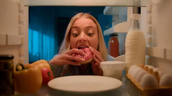 Buzdolabının içindeki POV bakış açısı. Akşam mutfağı açık beyaz kadın buzdolabı. Tatlı çörek, sağlıksız beslenme, obezite diyet, aşırı yemek bağımlılığı.