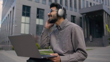 Arap Hintli bir adam müzik dinler kulaklıkla müzik eğitimi alır açık havada erkek iş adamı serbest çalışır dizüstü bilgisayarla iş projesi geliştirir şehirdeki gülümseyen çocuk e-öğrenimini internetten öğrenir