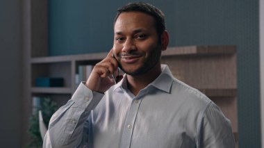 Şirketin işyerinde çalışan Amerikalı bir erkek ofis çalışanı cep telefonuyla konuşan, gülümseyen, çok kültürlü bir iş adamı iş görüşmesi yapan, kameralı telefondan gülümseyen telefonu tartışan.