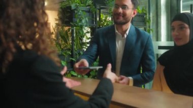 Arap Müslüman çift, tesettürlü erkek, turist, aile seyahati, mutlu ziyaretçiler otelin hizmet resepsiyonuna geliyor. Kadın kapıcı, anahtar pasaport kaydı yapıyor.